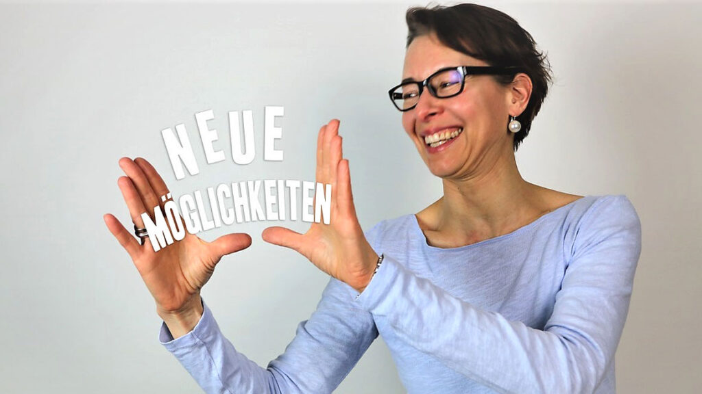 Daniela Gerlach lacht freundlich und hält visuell einen weißen Schriftzug in den offenen Händen, es steht dort "Neue Möglichkeiten".